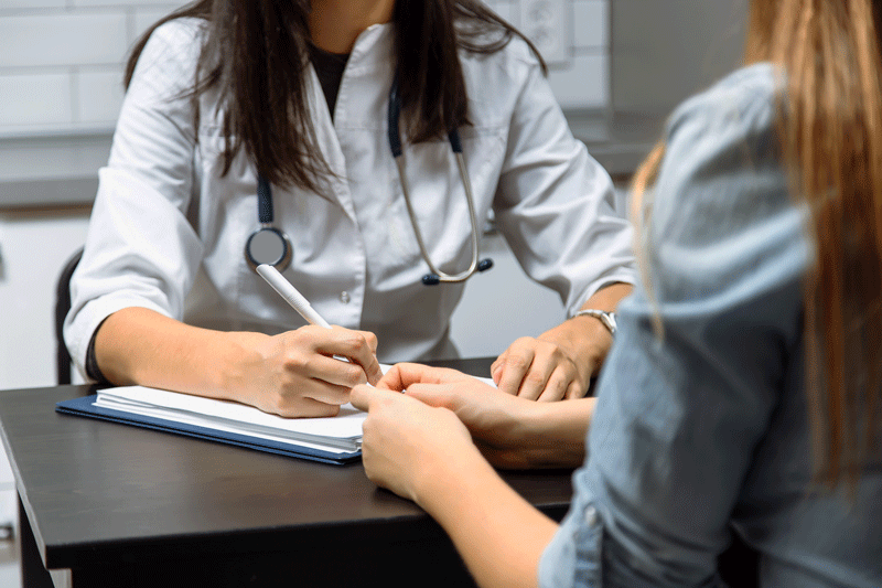 Close up of a female doctor filling up an application form while consulting patient